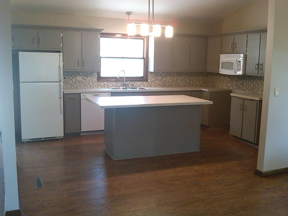 Open concept kitchen - mid-sized l-shaped laminate floor and brown floor open concept kitchen idea with a drop-in sink, flat-panel cabinets, gray cabinets, laminate countertops, beige backsplash, glass sheet backsplash, white appliances, an island and beige countertops