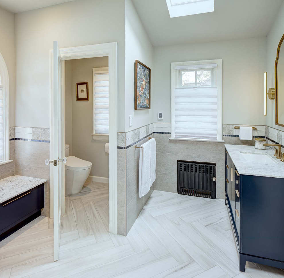 This is an example of a large eclectic master bathroom in New York with flat-panel cabinets, blue cabinets, an alcove shower, a bidet, gray tile, porcelain tile, grey walls, porcelain floors, marble benchtops, grey floor, a hinged shower door, white benchtops, a shower seat, a double vanity, a freestanding vanity and vaulted.
