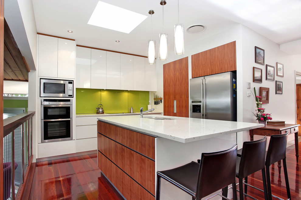 Inspiration for a contemporary l-shaped kitchen in Newcastle - Maitland with an undermount sink, flat-panel cabinets, white cabinets, green splashback, glass sheet splashback, stainless steel appliances, dark hardwood floors and with island.