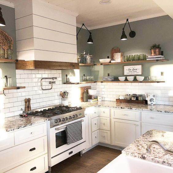 This is an example of a mid-sized country l-shaped eat-in kitchen in Columbus with a farmhouse sink, recessed-panel cabinets, white cabinets, granite benchtops, white splashback, subway tile splashback, white appliances, dark hardwood floors, with island, brown floor and grey benchtop.