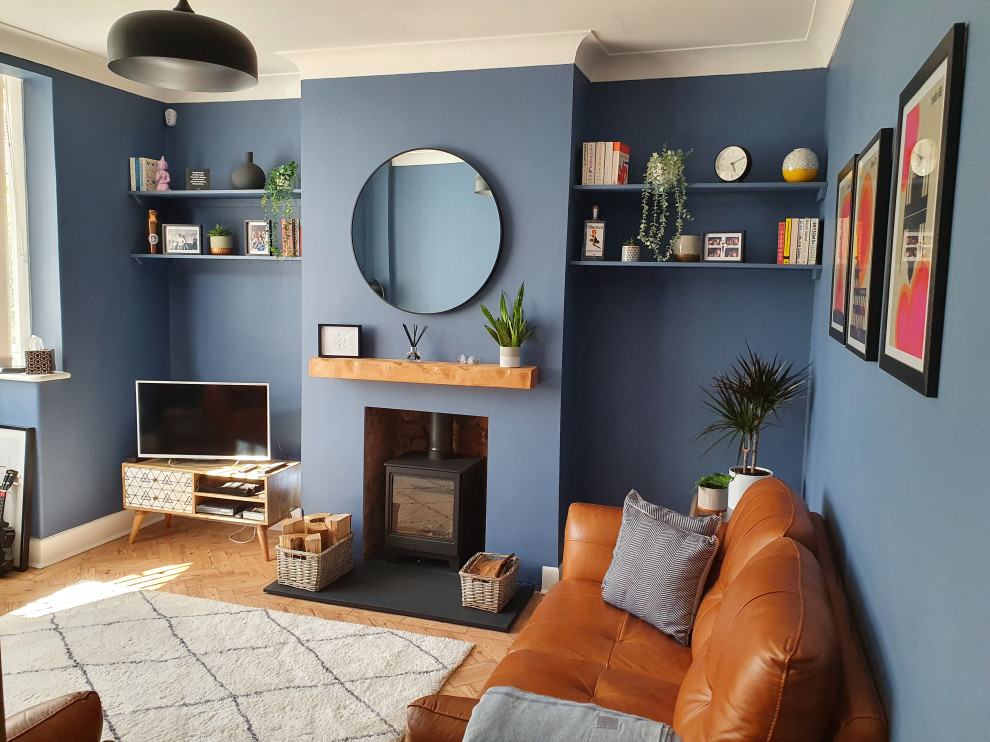 Inspiration för ett mellanstort funkis vardagsrum, med ett finrum, blå väggar, ljust trägolv, en öppen vedspis, en spiselkrans i tegelsten, en fristående TV och beiget golv