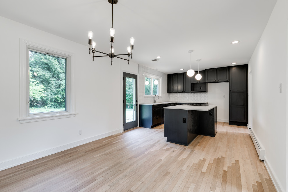 This is an example of a mid-sized midcentury l-shaped open plan kitchen in Richmond with raised-panel cabinets, black cabinets, white splashback, ceramic splashback, with island and white benchtop.