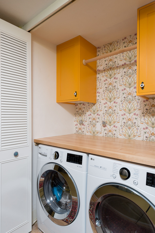 This is an example of a small traditional single-wall laundry cupboard in Portland with shaker cabinets, yellow cabinets, wood benchtops, white walls, laminate floors, a side-by-side washer and dryer, brown floor, brown benchtop and wallpaper.