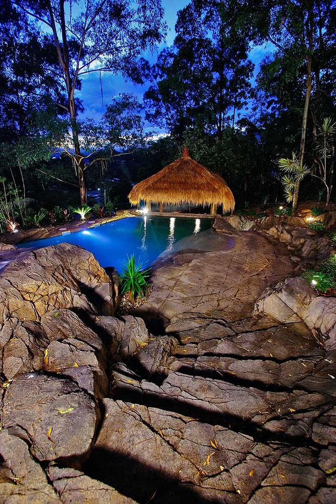 Mid-sized tropical front yard custom-shaped natural pool in Brisbane with a water slide and stamped concrete.