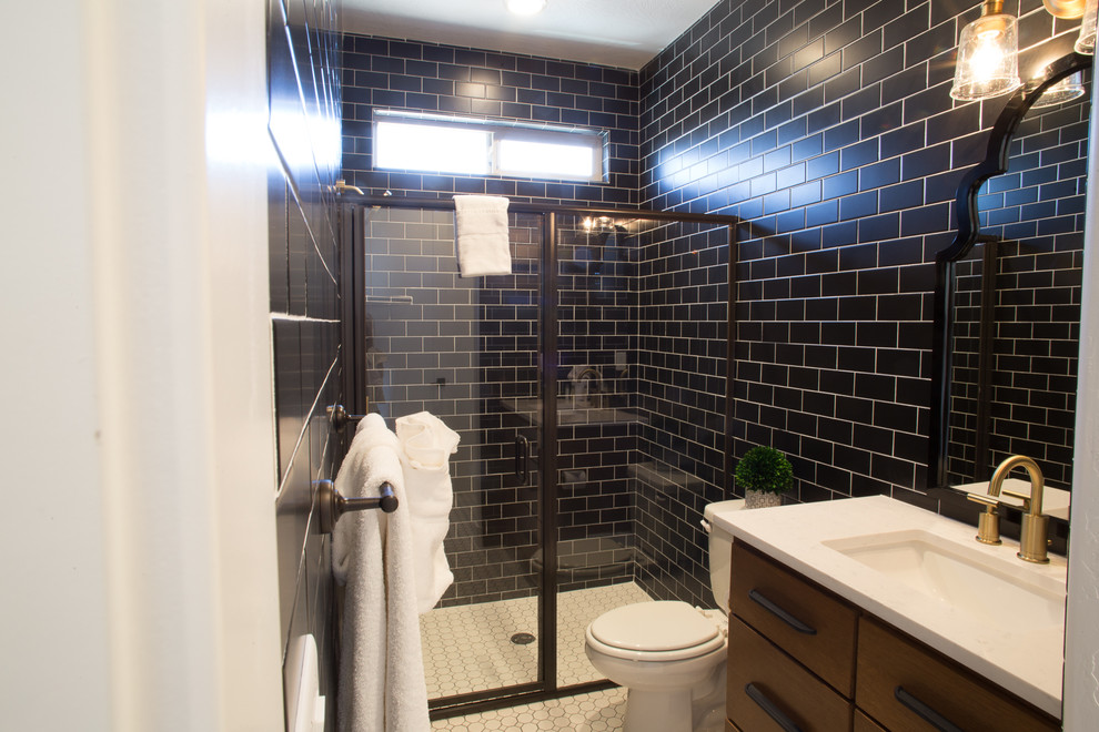 Inspiration for a mid-sized transitional bathroom in Salt Lake City with furniture-like cabinets, medium wood cabinets, an open shower, a two-piece toilet, black tile, subway tile, black walls, pebble tile floors, an undermount sink, engineered quartz benchtops, white floor, a hinged shower door and white benchtops.