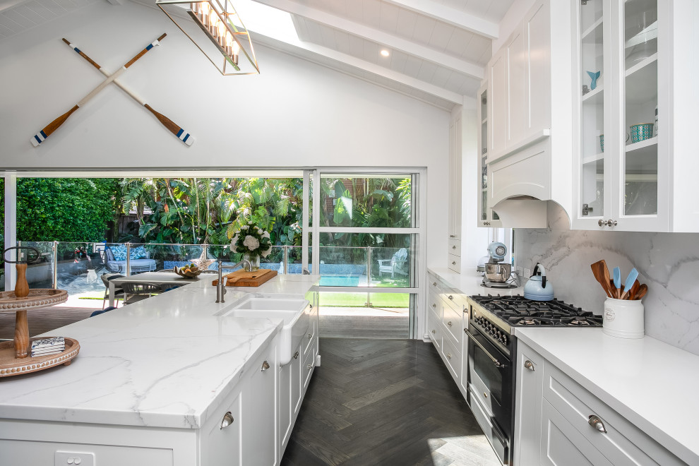 Large open plan kitchen in Sydney with a farmhouse sink, shaker cabinets, white cabinets, quartz benchtops, blue splashback, subway tile splashback, black appliances, dark hardwood floors, with island, black floor and exposed beam.