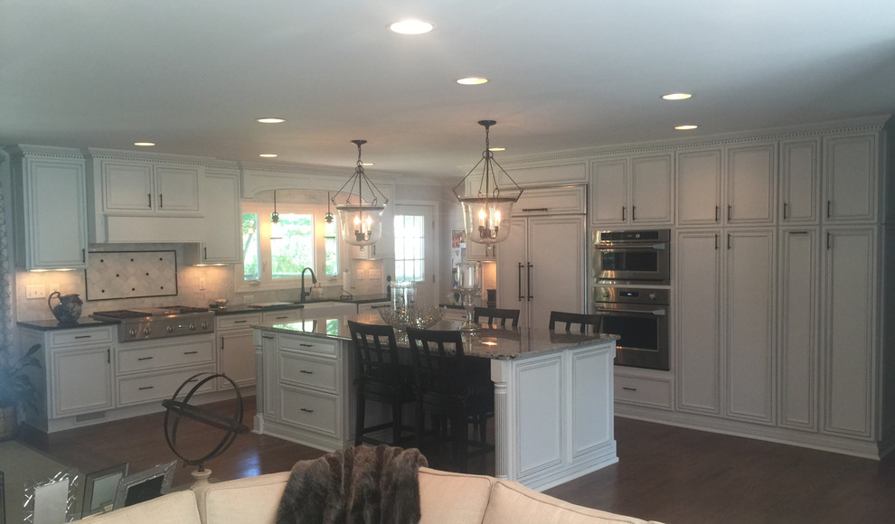 Eat-in kitchen - large transitional l-shaped dark wood floor eat-in kitchen idea in Baltimore with a farmhouse sink, flat-panel cabinets, white cabinets, granite countertops, white backsplash, stone tile backsplash, paneled appliances and an island