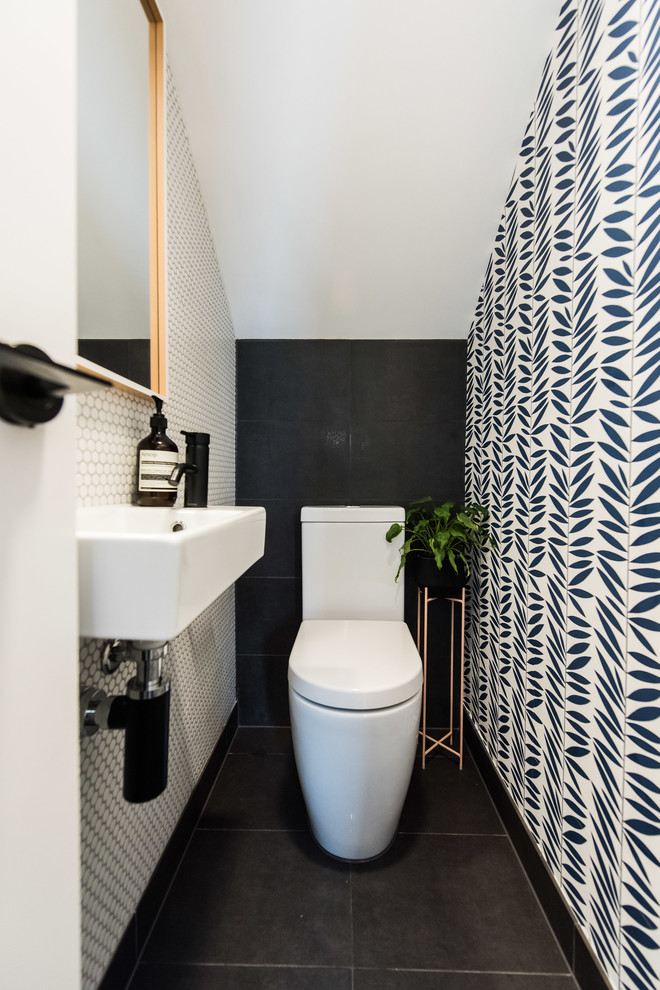 This is an example of a contemporary powder room in Melbourne with a one-piece toilet, mosaic tile, porcelain floors, a wall-mount sink, black floor, white tile and multi-coloured walls.