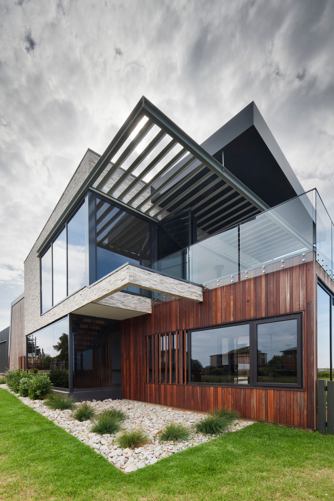 This is an example of a large contemporary two-storey house exterior in Melbourne with wood siding, a flat roof and a metal roof.