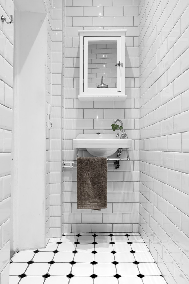 Inspiration for a small scandinavian powder room in Stockholm with white cabinets, white tile, white walls, a wall-mount sink, subway tile and multi-coloured floor.