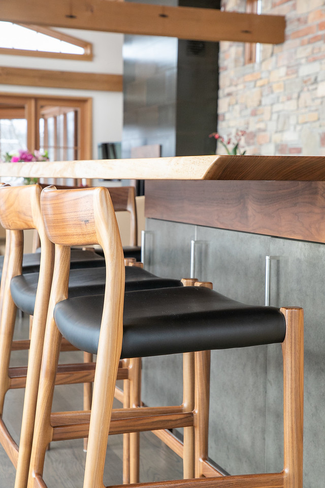 Large mountain style l-shaped medium tone wood floor and brown floor open concept kitchen photo with flat-panel cabinets, light wood cabinets, granite countertops, black backsplash, stainless steel appliances, an island, black countertops, a double-bowl sink and porcelain backsplash
