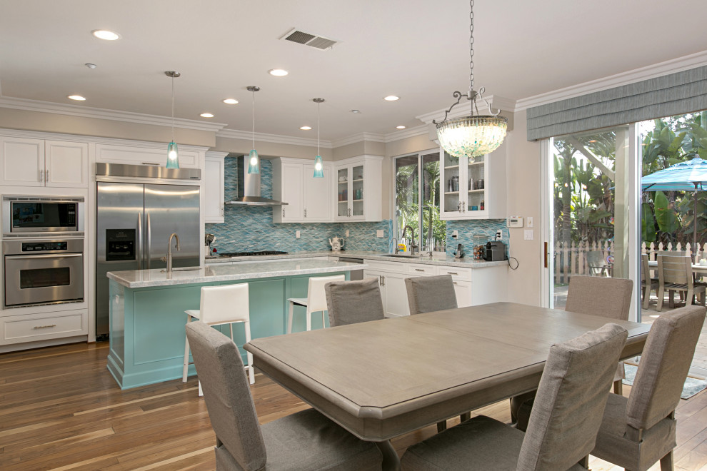 This is an example of a large beach style l-shaped open plan kitchen in San Diego with a single-bowl sink, recessed-panel cabinets, turquoise cabinets, quartzite benchtops, blue splashback, glass tile splashback, stainless steel appliances, medium hardwood floors, with island, brown floor and white benchtop.