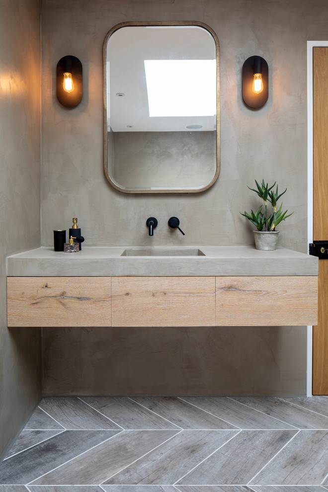This is an example of an eclectic bathroom in London with flat-panel cabinets, grey cabinets, a wall-mount toilet, grey walls, porcelain floors, a drop-in sink, concrete benchtops, grey floor, an open shower and grey benchtops.