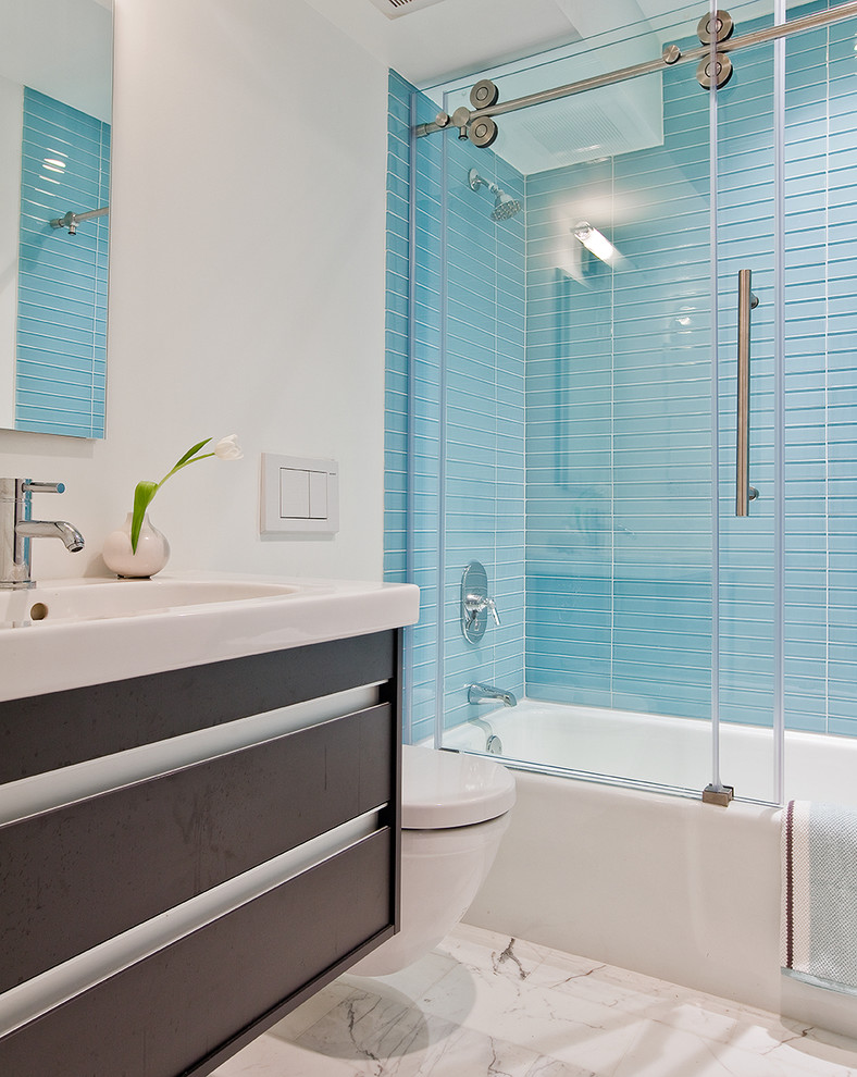 This is an example of a mid-sized contemporary master bathroom in Boston with a shower/bathtub combo, a wall-mount toilet, blue tile, glass tile, flat-panel cabinets, dark wood cabinets, an alcove tub, white walls, marble floors, an integrated sink and engineered quartz benchtops.