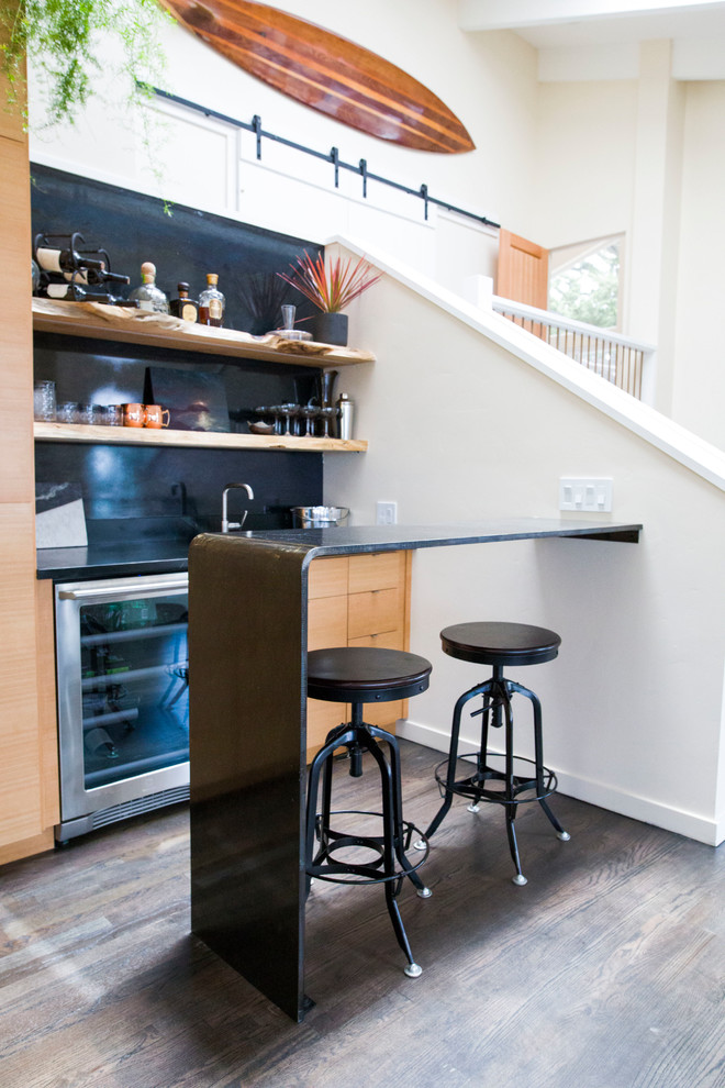 Small modern galley seated home bar in Other with an undermount sink, open cabinets, light wood cabinets, soapstone benchtops, black splashback, medium hardwood floors, grey floor and black benchtop.