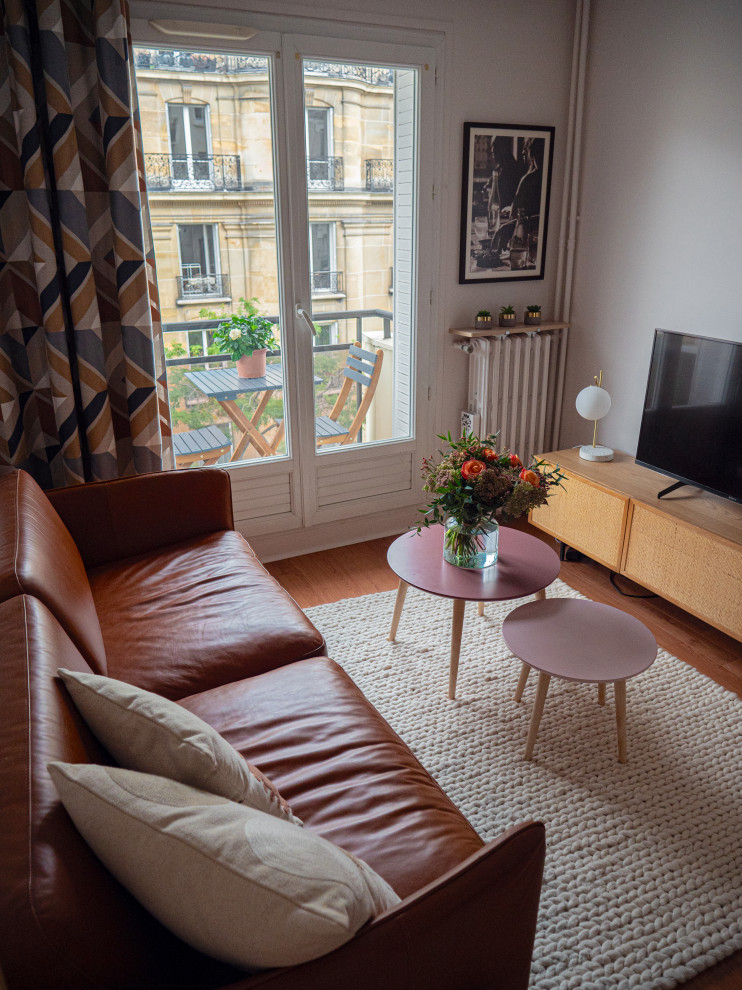 Стильный дизайн: изолированная гостиная комната среднего размера в современном стиле с белыми стенами, полом из ламината, отдельно стоящим телевизором и коричневым полом - последний тренд