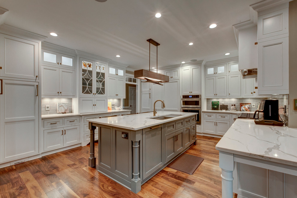 Large transitional u-shaped open plan kitchen in Raleigh with beaded inset cabinets, white cabinets, grey splashback, dark hardwood floors, with island, panelled appliances, marble benchtops, subway tile splashback and an undermount sink.
