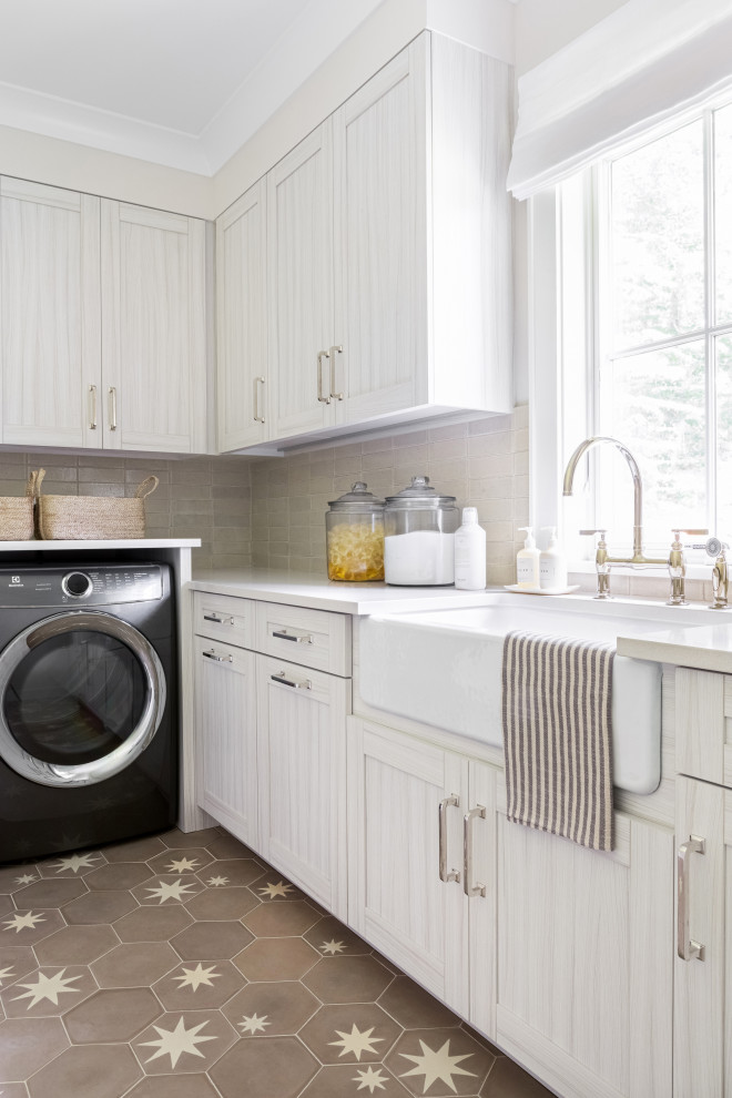Large transitional l-shaped dedicated laundry room in New York with a farmhouse sink, recessed-panel cabinets, light wood cabinets, marble benchtops, beige walls, ceramic floors, a side-by-side washer and dryer, brown floor and beige benchtop.