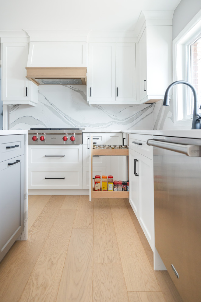 Eat-in kitchen - mid-sized transitional u-shaped light wood floor eat-in kitchen idea in Toronto with an undermount sink, shaker cabinets, white cabinets, quartz countertops, white backsplash, quartz backsplash, stainless steel appliances, an island and white countertops