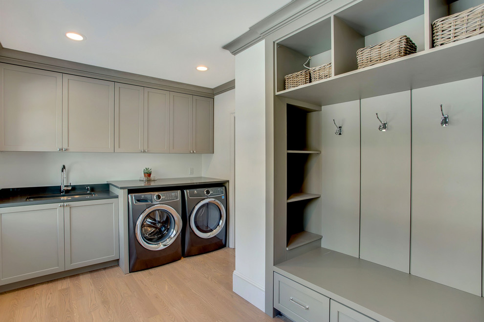 Inspiration for a large contemporary galley utility room in New York with a drop-in sink, shaker cabinets, green cabinets, green walls, light hardwood floors, a side-by-side washer and dryer, brown floor and black benchtop.