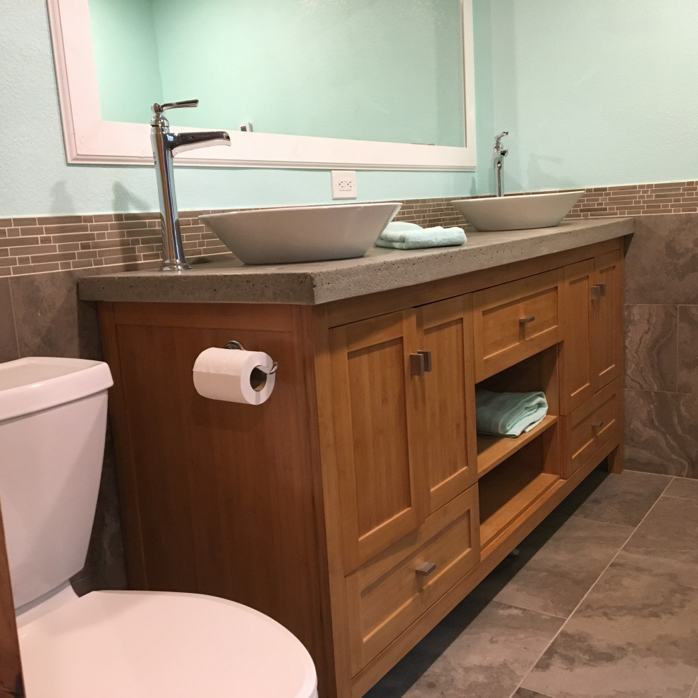 This is an example of a large modern master bathroom in Orlando with shaker cabinets, medium wood cabinets, a freestanding tub, a double shower, a two-piece toilet, brown tile, limestone, blue walls, limestone floors, a vessel sink, concrete benchtops, brown floor, a sliding shower screen and grey benchtops.