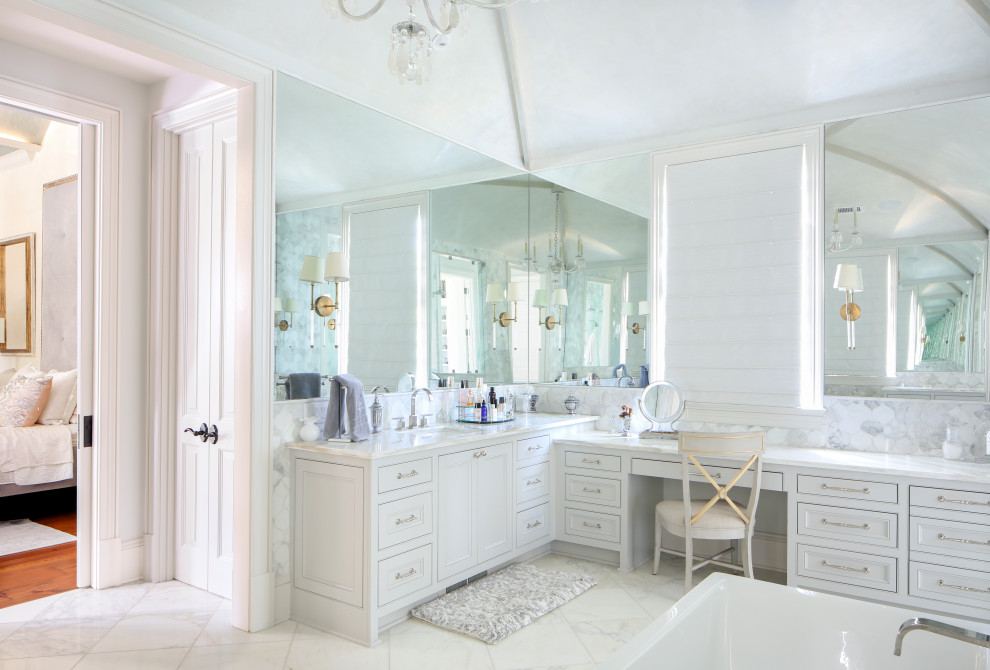 Photo of an expansive transitional master bathroom in New Orleans with white cabinets, a freestanding tub, an open shower, gray tile, white walls, an undermount sink, white floor, white benchtops, a laundry, a double vanity, a built-in vanity and vaulted.