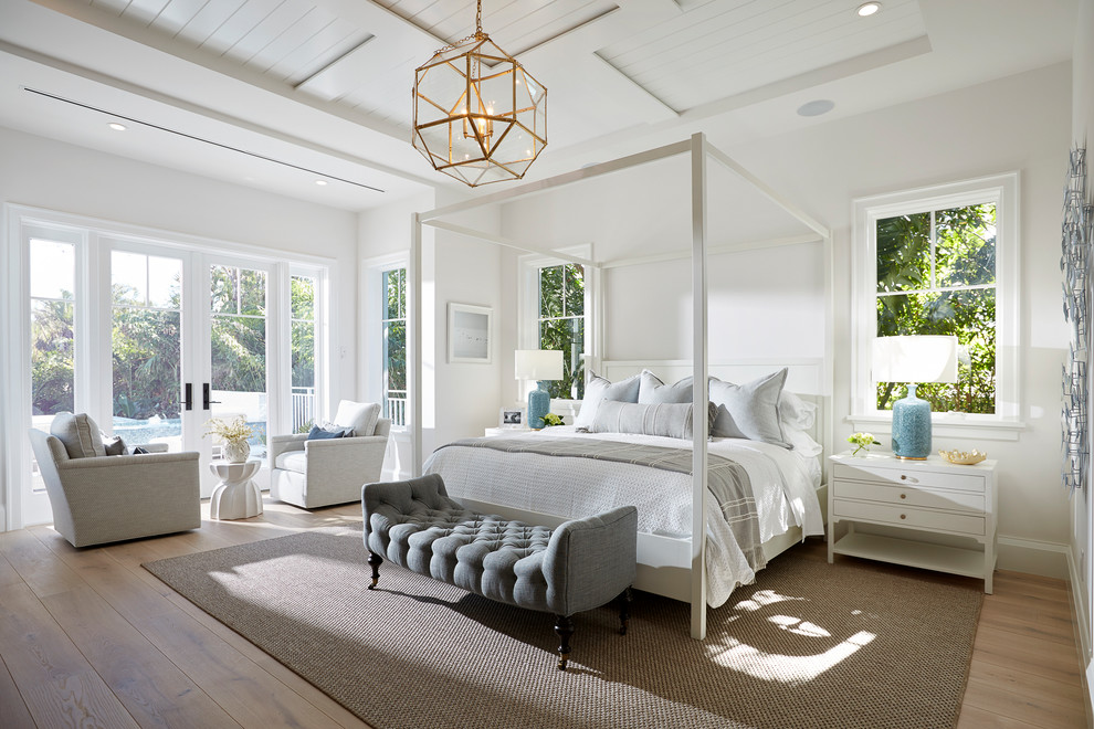 This is an example of a beach style master bedroom in Miami with white walls, medium hardwood floors and brown floor.