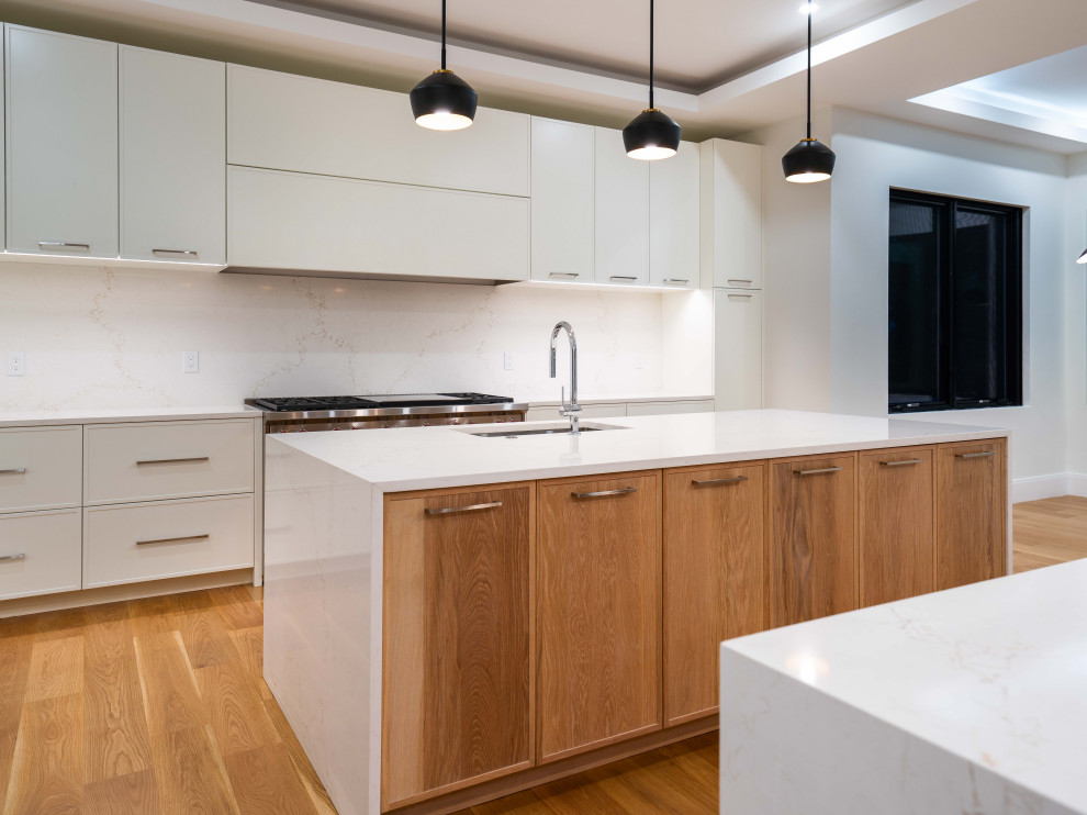 Example of a transitional light wood floor and tray ceiling kitchen design in Boston with an undermount sink, shaker cabinets, quartz countertops, quartz backsplash, stainless steel appliances and two islands