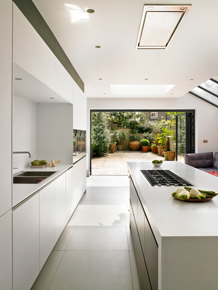 This is an example of a large contemporary single-wall open plan kitchen in London with a double-bowl sink, flat-panel cabinets, white cabinets, with island, ceramic floors and beige floor.