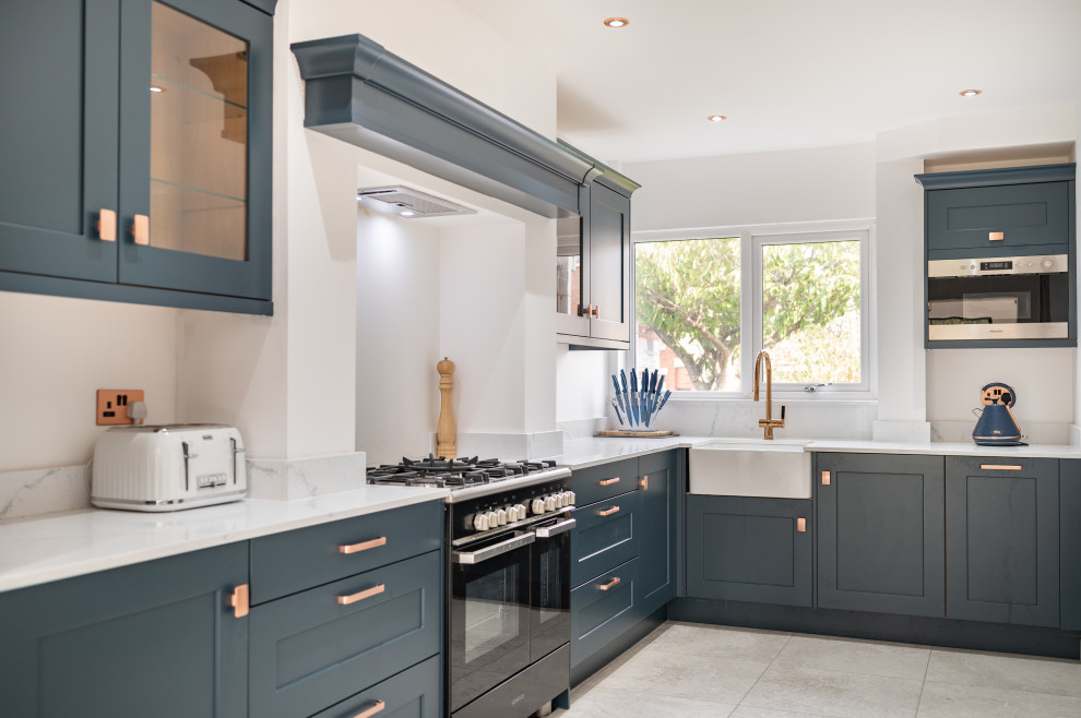 Traditional l-shaped kitchen in Other with a belfast sink, shaker cabinets, grey cabinets, black appliances, grey floors and white worktops.