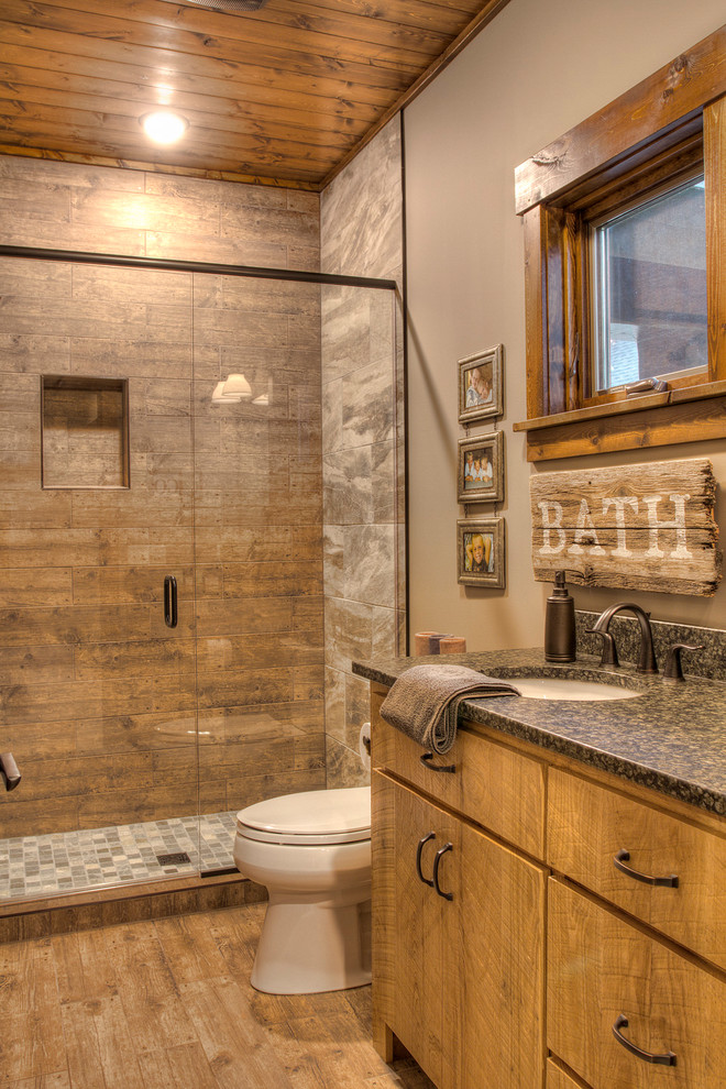 Inspiration for a country bathroom in Minneapolis with flat-panel cabinets, medium wood cabinets, an alcove shower, brown tile, grey walls, medium hardwood floors, an undermount sink, brown floor, a hinged shower door and black benchtops.