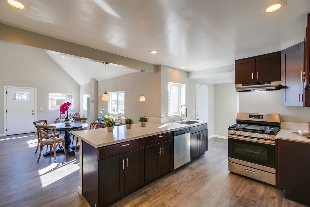 Photo of a small eclectic u-shaped eat-in kitchen in San Diego with an undermount sink, shaker cabinets, dark wood cabinets, quartz benchtops, white splashback, stainless steel appliances, laminate floors and a peninsula.