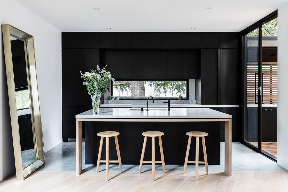 Design ideas for a large contemporary galley open plan kitchen in Melbourne with a double-bowl sink, recessed-panel cabinets, black cabinets, quartz benchtops, grey splashback, glass sheet splashback, black appliances, cement tiles, with island and grey floor.