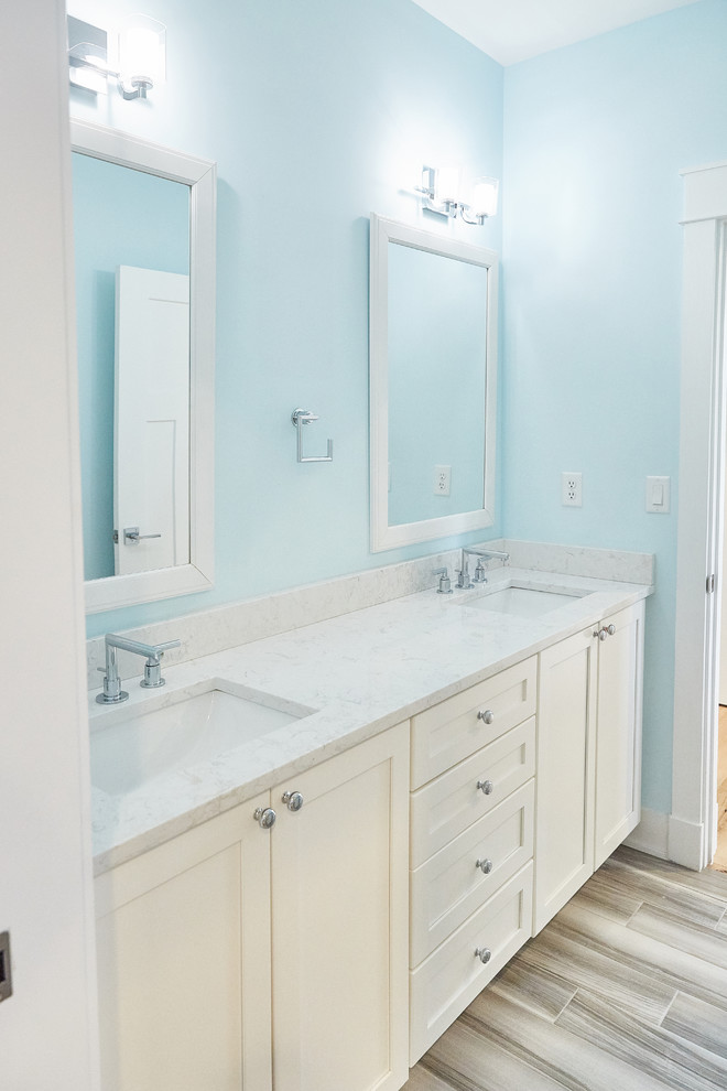 Photo of a mid-sized beach style bathroom in Other with shaker cabinets, white cabinets, an alcove tub, a shower/bathtub combo, gray tile, porcelain tile, blue walls, porcelain floors, an undermount sink, grey floor, a sliding shower screen and white benchtops.