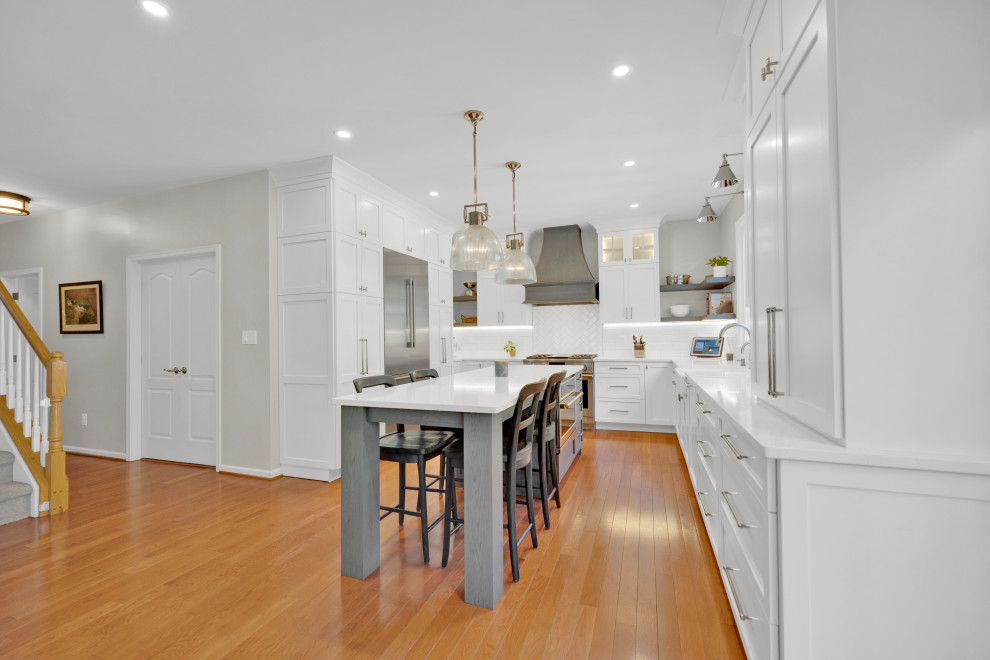 Design ideas for a mid-sized transitional galley kitchen in DC Metro with an undermount sink, shaker cabinets, white cabinets, quartz benchtops, white splashback, cement tile splashback, stainless steel appliances, medium hardwood floors, with island, yellow floor and white benchtop.