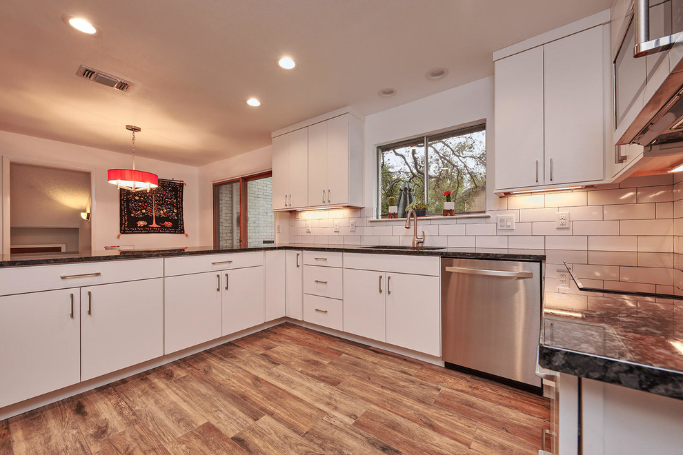 This is an example of a mid-sized transitional u-shaped eat-in kitchen in Austin with an undermount sink, flat-panel cabinets, white cabinets, granite benchtops, white splashback, stainless steel appliances, porcelain floors, a peninsula, brown floor and subway tile splashback.