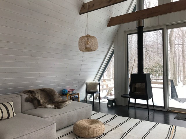 This is an example of a small country loft-style living room in New York with white walls, a wood stove and black floor.