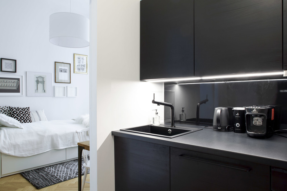 This is an example of a small modern single-wall separate kitchen in Berlin with an integrated sink, louvered cabinets, black cabinets, laminate benchtops, black splashback, metal splashback, black appliances, medium hardwood floors, no island and brown floor.