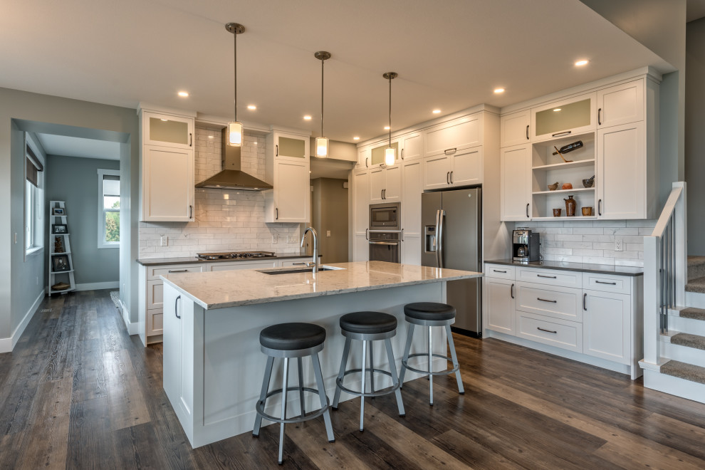 Photo of a mid-sized transitional u-shaped open plan kitchen in Other with an undermount sink, shaker cabinets, white cabinets, quartzite benchtops, white splashback, subway tile splashback, stainless steel appliances, laminate floors, with island, brown floor and white benchtop.