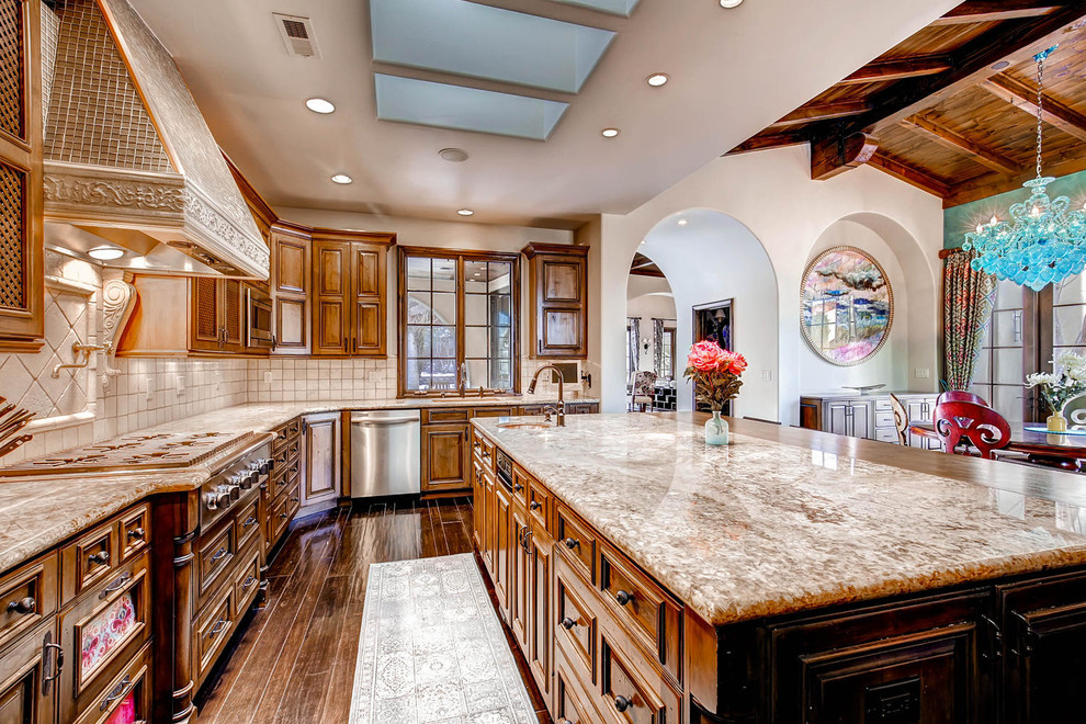 This is an example of a large mediterranean u-shaped open plan kitchen in Denver with an undermount sink, raised-panel cabinets, medium wood cabinets, granite benchtops, beige splashback, stone tile splashback, panelled appliances and with island.