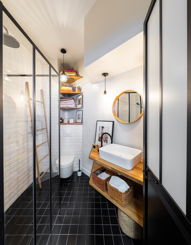 Design ideas for a small contemporary 3/4 bathroom in Paris with a curbless shower, a wall-mount toilet, subway tile, white walls, cement tiles, wood benchtops, black floor, open cabinets, medium wood cabinets, white tile, a vessel sink, an open shower and beige benchtops.