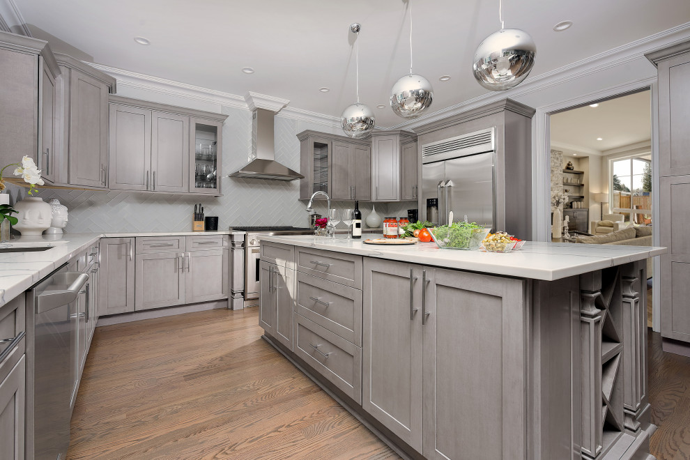 This is an example of a medium sized classic u-shaped kitchen/diner in Chicago with a submerged sink, flat-panel cabinets, grey cabinets, engineered stone countertops, white splashback, glass tiled splashback, stainless steel appliances, medium hardwood flooring, an island and white worktops.