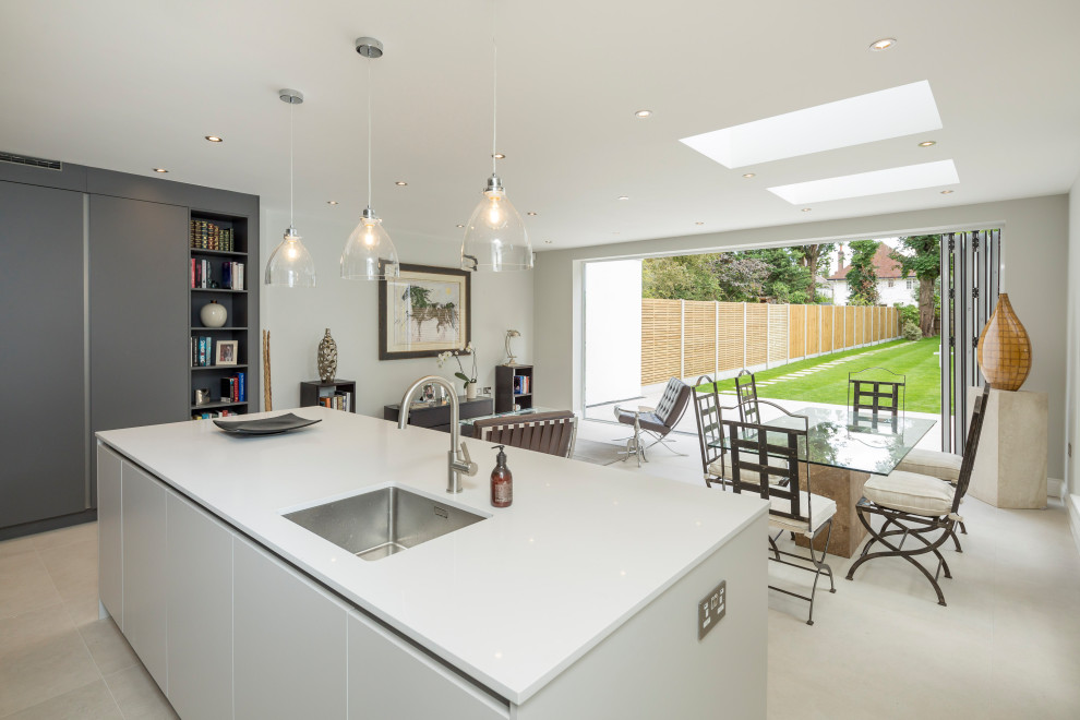 Photo of a large contemporary l-shaped open plan kitchen in London with a drop-in sink, flat-panel cabinets, grey cabinets, quartzite benchtops, black appliances, with island and white benchtop.