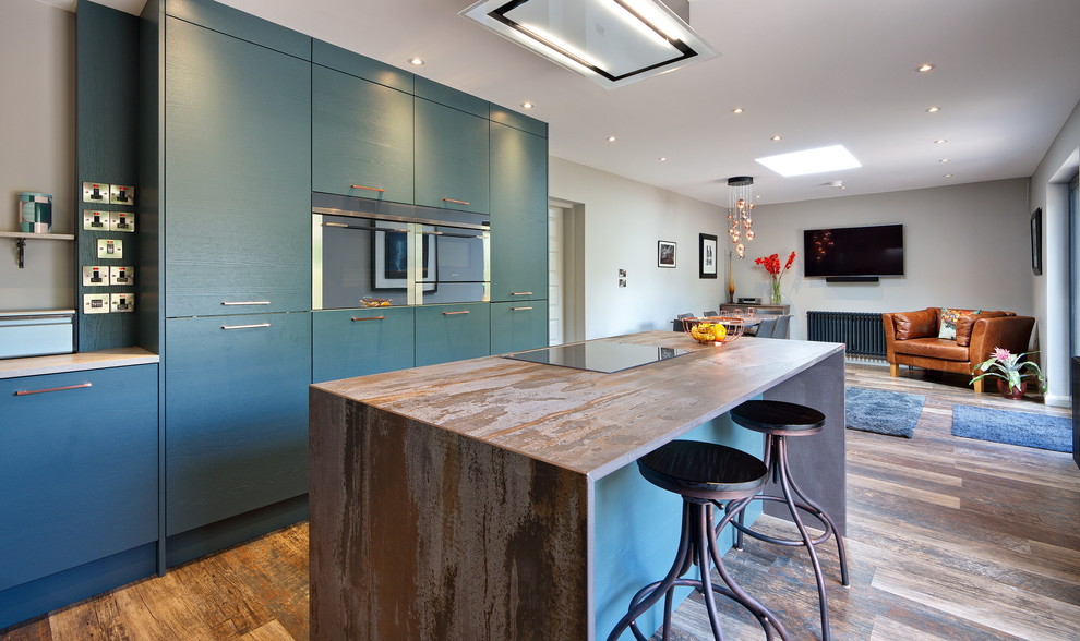 Inspiration for a mid-sized contemporary l-shaped open plan kitchen in Other with a drop-in sink, flat-panel cabinets, green cabinets, tile benchtops, grey splashback, timber splashback, stainless steel appliances, laminate floors, with island, brown floor and brown benchtop.
