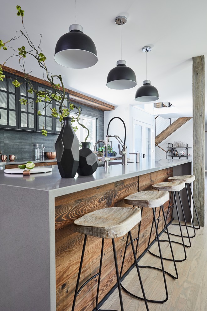 Mid-sized modern single-wall open plan kitchen in New York with a drop-in sink, dark wood cabinets, concrete benchtops, black splashback, stone tile splashback, panelled appliances, light hardwood floors, with island, grey floor, grey benchtop and glass-front cabinets.