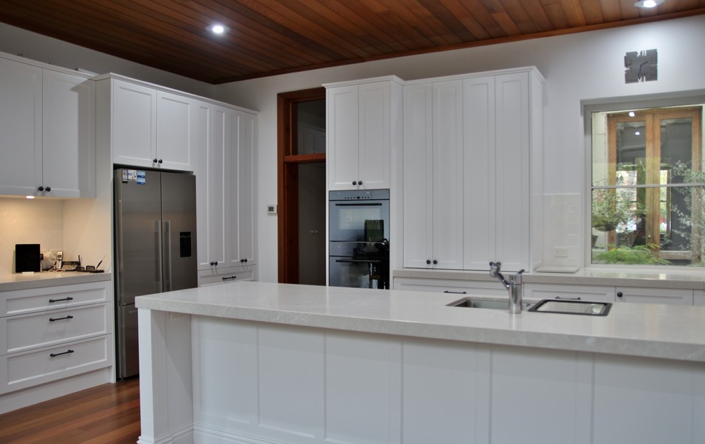 Large traditional u-shaped eat-in kitchen in Melbourne with an undermount sink, recessed-panel cabinets, white cabinets, quartz benchtops, white splashback, ceramic splashback, stainless steel appliances, medium hardwood floors and no island.