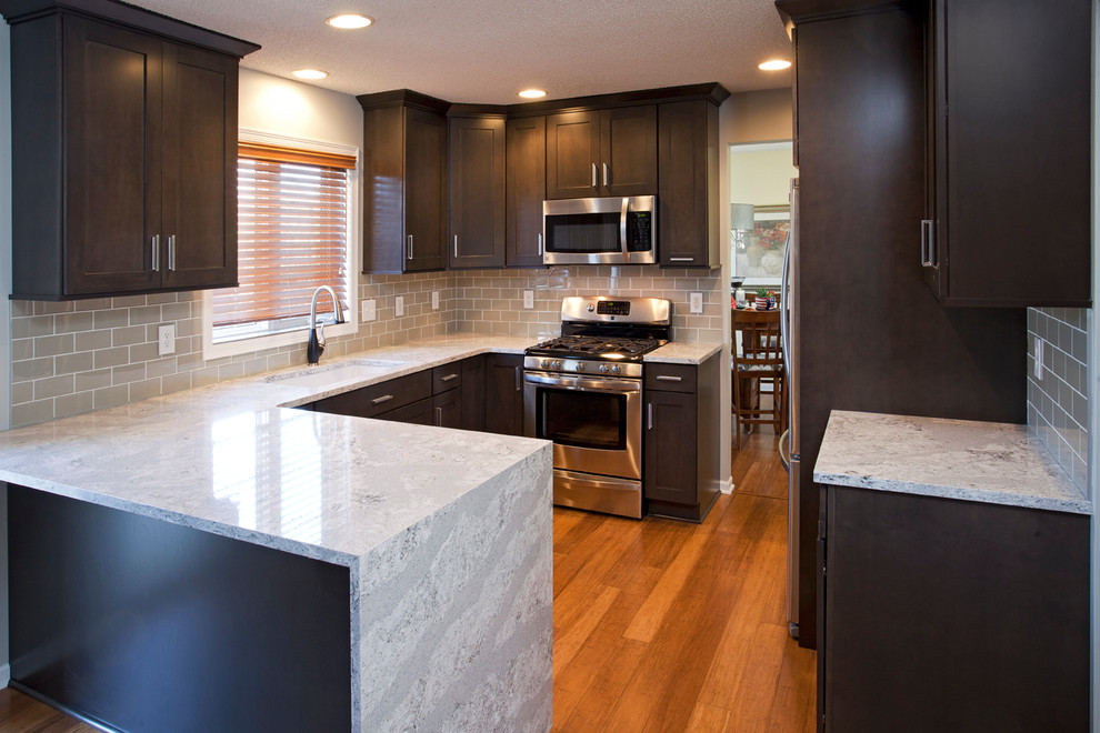Mid-sized transitional u-shaped medium tone wood floor eat-in kitchen photo in Minneapolis with an undermount sink, flat-panel cabinets, dark wood cabinets, gray backsplash, glass tile backsplash, stainless steel appliances and a peninsula