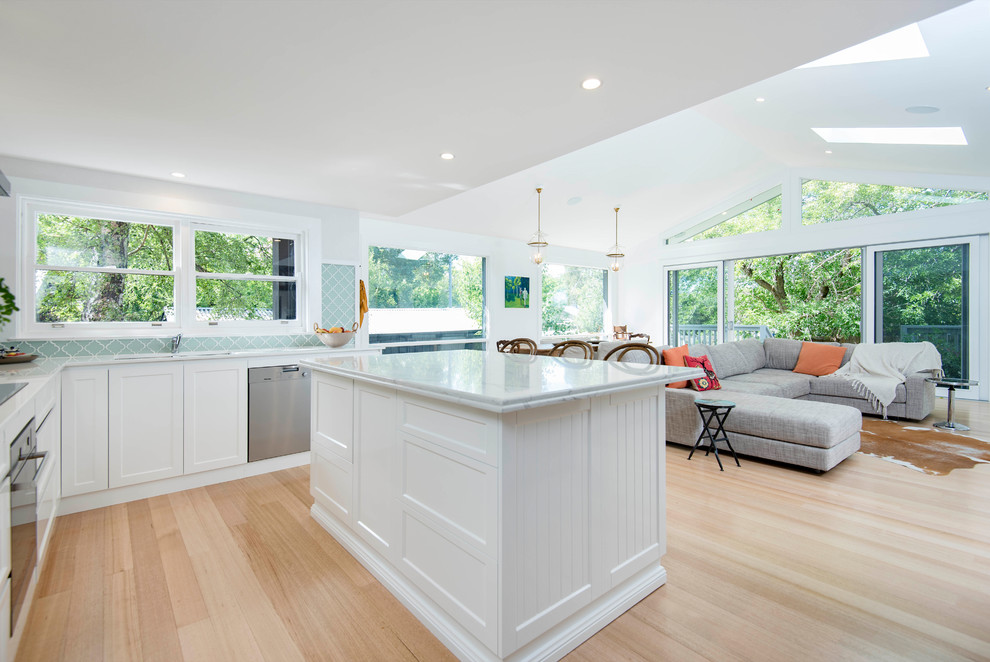 This is an example of a mid-sized contemporary l-shaped open plan kitchen in Canberra - Queanbeyan with a drop-in sink, shaker cabinets, white cabinets, marble benchtops, green splashback, porcelain splashback, stainless steel appliances, light hardwood floors and with island.
