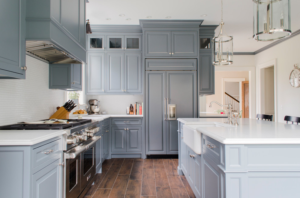 Inspiration for a traditional l-shaped kitchen in Cleveland with a farmhouse sink, raised-panel cabinets, grey cabinets, white splashback, mosaic tile splashback, panelled appliances, with island and brown floor.