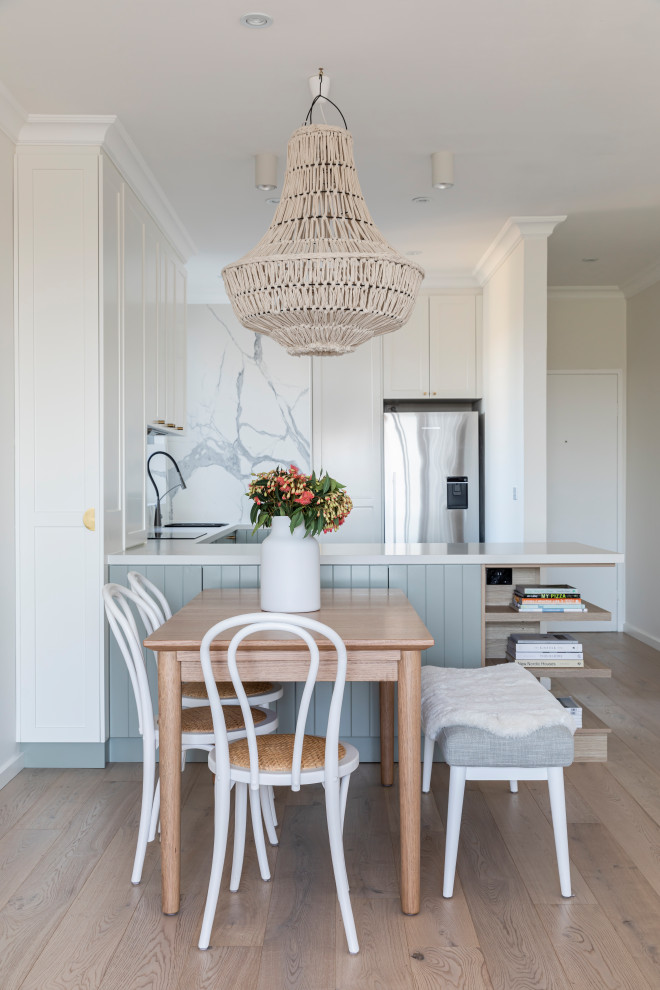 Design ideas for a small beach style u-shaped eat-in kitchen in Sydney with an undermount sink, shaker cabinets, white cabinets, quartz benchtops, white splashback, marble splashback, stainless steel appliances, light hardwood floors, no island, brown floor and white benchtop.